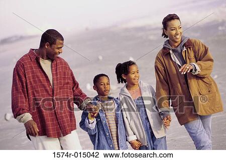 Stock Image - Parents and their two children walking on the beach. Fotosearch