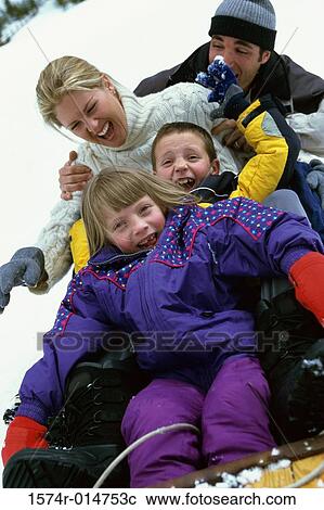Stock Image - Parents with their son and daughter sliding down a hill on a toboggan. Fotosearch