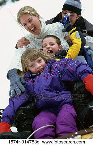 Stock Image - Parents with their son and daughter sliding down a hill on a toboggan. Fotosearch