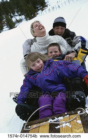 Stock Image - Parents with their son and daughter sliding down a hill on a toboggan. Fotosearch