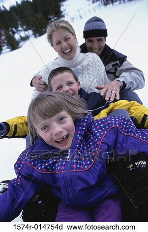 Stock Image - Parents with their son and daughter sliding down a hill on a toboggan. Fotosearch