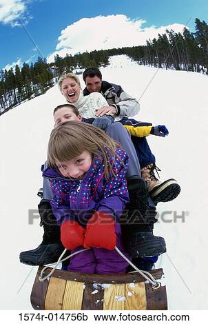 Stock Image - Parents with their son and daughter sliding down a hill on a toboggan. Fotosearch