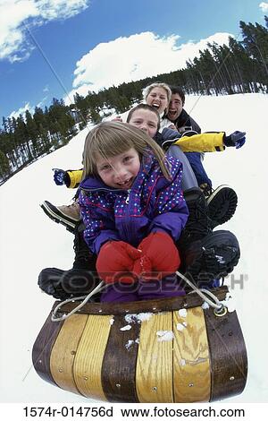 Stock Image - Parents with their son and daughter sliding down a hill on a toboggan. Fotosearch