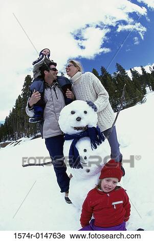 Stock Image - Parents with their son and daughter near a snowman. Fotosearch