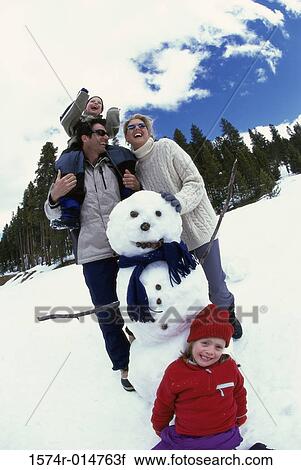 Stock Image - Parents with their son and daughter near a snowman. Fotosearch