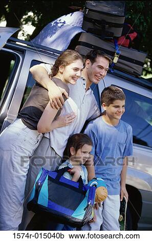 Stock Image - Parents with their son and daughter standing beside a car. Fotosearch