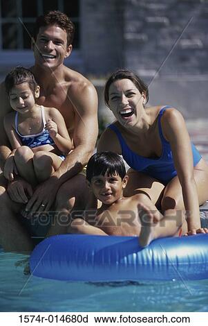Stock Image - Parents with their two children sitting at the poolside. Fotosearch