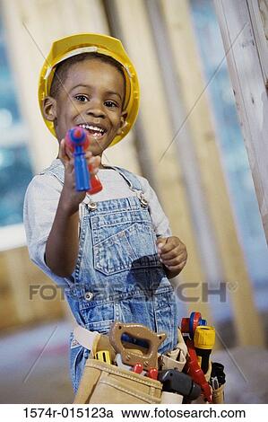 Stock Image - Portrait of a boy dressed as a construction worker holding a toy drill. Fotosearch