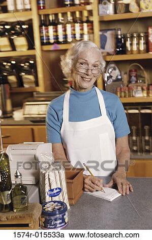 Stock Image - Portrait of a female sales clerk writing on a note pad in a store. Fotosearch