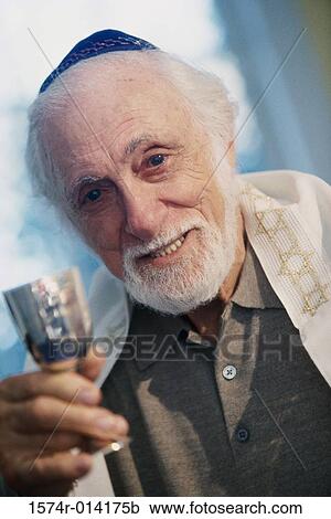 Stock Image - Portrait of a senior man holding a goblet at a Hanukkah ceremony. Fotosearch
