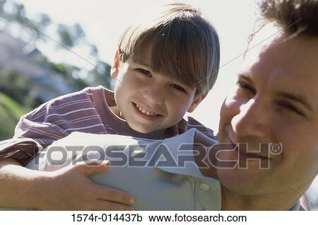 Stock Image - Portrait of a son hugging his father from behind. Fotosearch