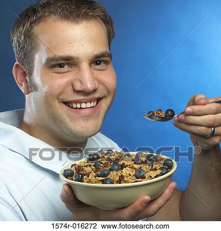 Stock Image - Portrait of a young man holding a bowl of corn flakes smiling. Fotosearch