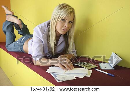 Stock Image - Portrait of a young woman lying on a bench with bills and a calculator in front of her. Fotosearch