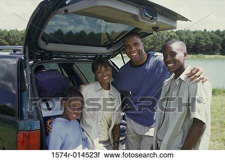 Stock Image - Portrait of parents behind a car with their son and daughter. Fotosearch