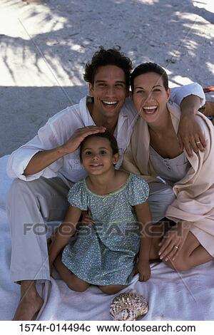 Stock Image - Portrait of parents sitting with their daughter on the beach. Fotosearch
