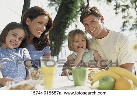 Stock Image - Portrait of two sisters sitting with their parents and smiling. Fotosearch