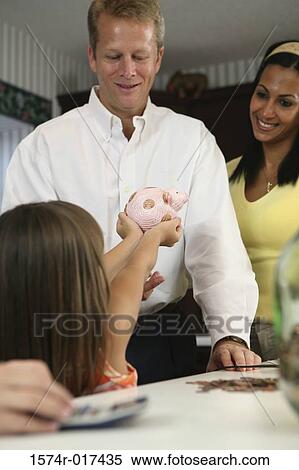 Stock Photography - Rear view of a daughter showing a piggy bank to her parents. Fotosearch