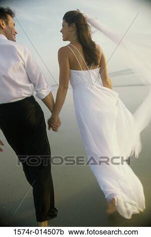 Stock Image - Rear view of a newlywed couple on the beach. Fotosearch