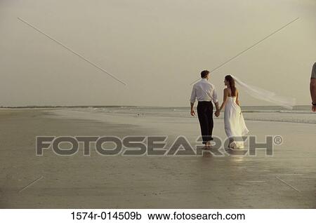 Stock Image - Rear view of a newlywed couple walking on the beach. Fotosearch