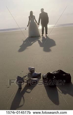 Stock Image - Rear view of a newlywed couple walking on the beach. Fotosearch