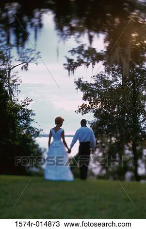 Stock Image - Rear view of a newlywed couple walking in a park. Fotosearch