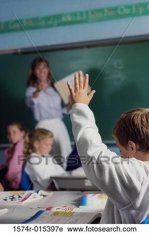 Rear view of a schoolboy raising his hand in a classroom View Large Photo Image Stock Image - Rear view of a schoolboy raising his hand in a classroom. Fotosearch