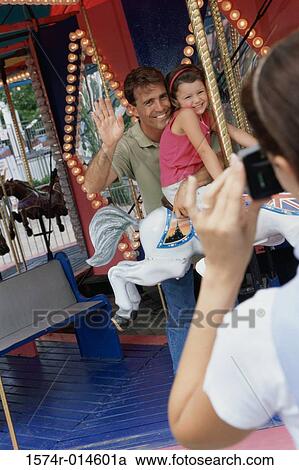Rear view of a woman taking a photograph of her husband and daughter sitting on a carousel horse View Large Photo Image Stock Image - Rear view of a woman taking a photograph of her husband and daughter sitting on a carousel horse. Fotosearch