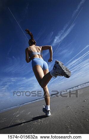 Stock Image - Rear view of a young woman jogging on the beach. Fotosearch