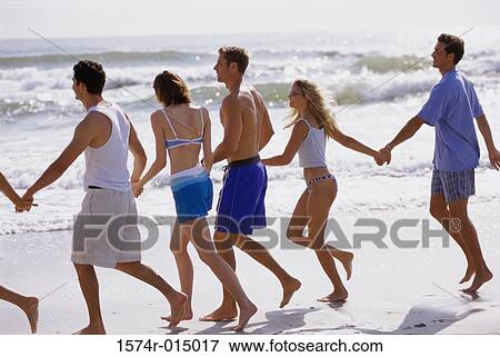 Stock Photo - Rear view of young men and young women holding hands running on the beach. Fotosearch