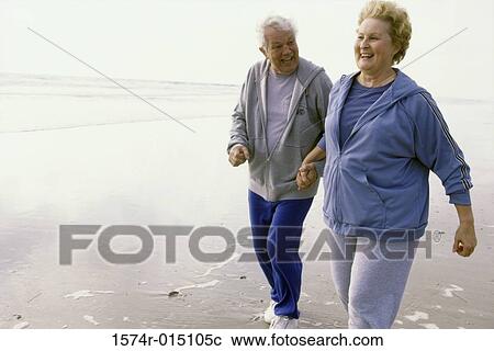 Stock Image - Senior couple jogging on the beach. Fotosearch