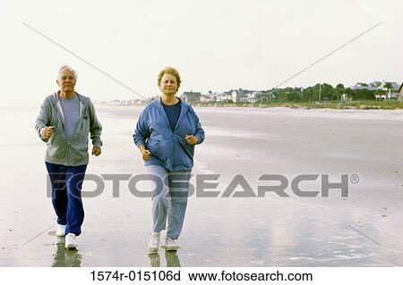Stock Image - Senior couple jogging on the beach. Fotosearch