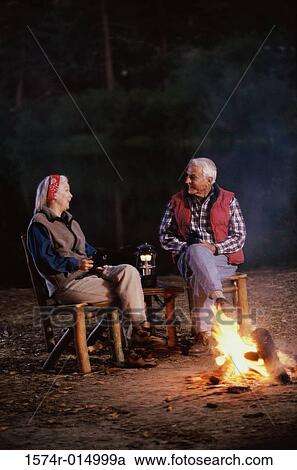 Stock Image - Senior couple sitting near a campfire talking to each other. Fotosearch