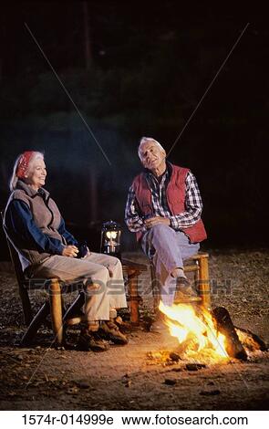 Stock Image - Senior couple sitting near a campfire talking to each other. Fotosearch