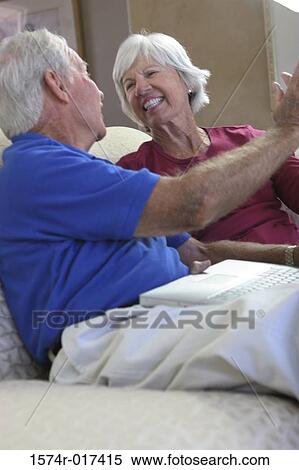Stock Photography - Senior couple sitting on a couch smiling. Fotosearch