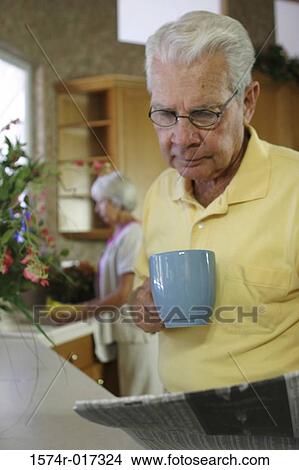 Senior man holding a coffee cup reading a newspaper View Large Photo Image Picture - Senior man holding a coffee cup reading a newspaper. Fotosearch