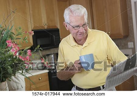 Picture - Senior man holding a coffee cup reading a newspaper. Fotosearch