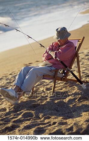 Senior man sitting on the beach in a deck chair with a fishing rod View Large Photo Image Stock Image - Senior man sitting on the beach in a deck chair with a fishing rod. Fotosearch