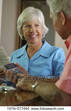 Senior man using a calculator with a senior woman sitting beside him View Large Photo Image Picture - Senior man using a calculator with a senior woman sitting beside him. Fotosearch