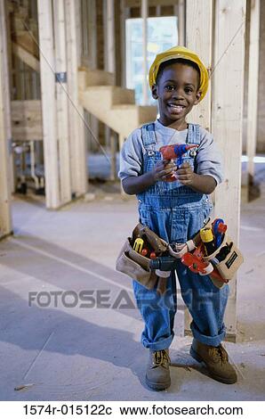 Stock Image - Side profile of a boy dressed as a construction worker holding a toy drill. Fotosearch