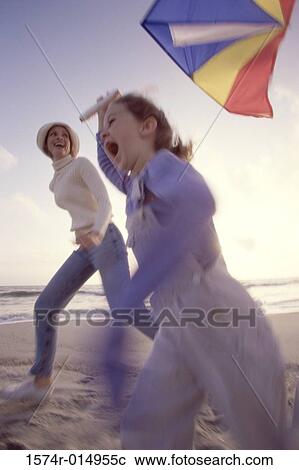 Stock Image - Side profile of a daughter flying a kite with her mother on the beach. Fotosearch