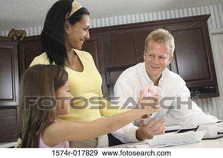 Stock Photo - Side profile of a daughter showing a piggy bank to her parents. Fotosearch