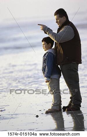 Stock Image - Side profile of a father and son standing on the beach. Fotosearch