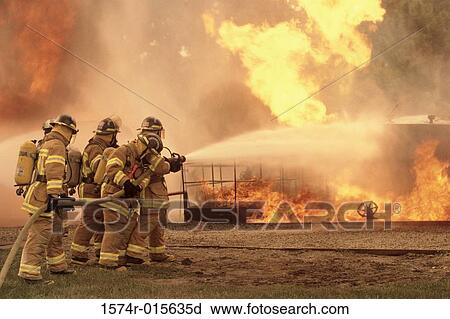 Stock Image - Side profile of a group of firefighters holding water hoses. Fotosearch