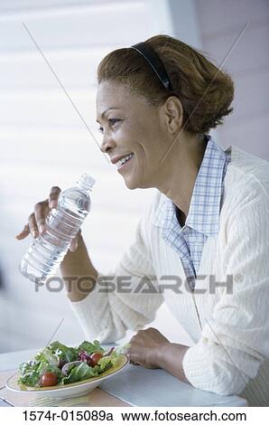 Stock Image - Side profile of a mid adult woman drinking water from a water bottle. Fotosearch