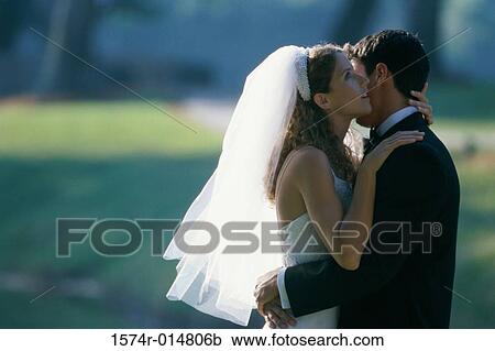 Stock Image - Side profile of a newlywed couple embracing each other. Fotosearch