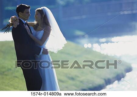 Stock Image - Side profile of a newlywed couple embracing each other. Fotosearch