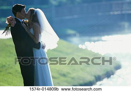 Stock Image - Side profile of a newlywed couple kissing each other. Fotosearch