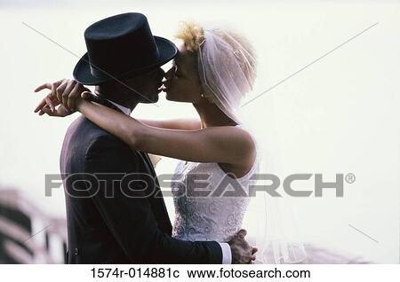 Stock Image - Side profile of a newlywed couple kissing each other. Fotosearch