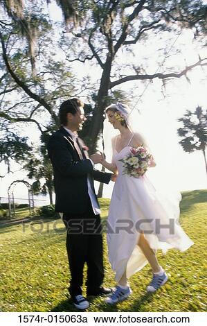 Stock Image - Side profile of a newlywed couple standing in a park. Fotosearch