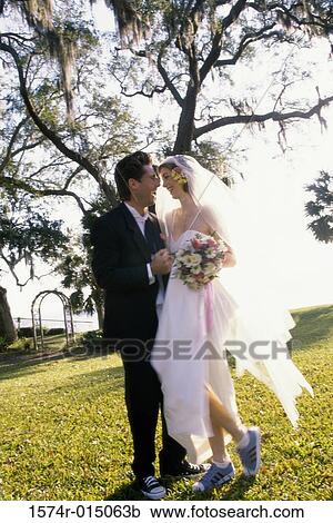 Stock Image - Side profile of a newlywed couple standing in a park. Fotosearch
